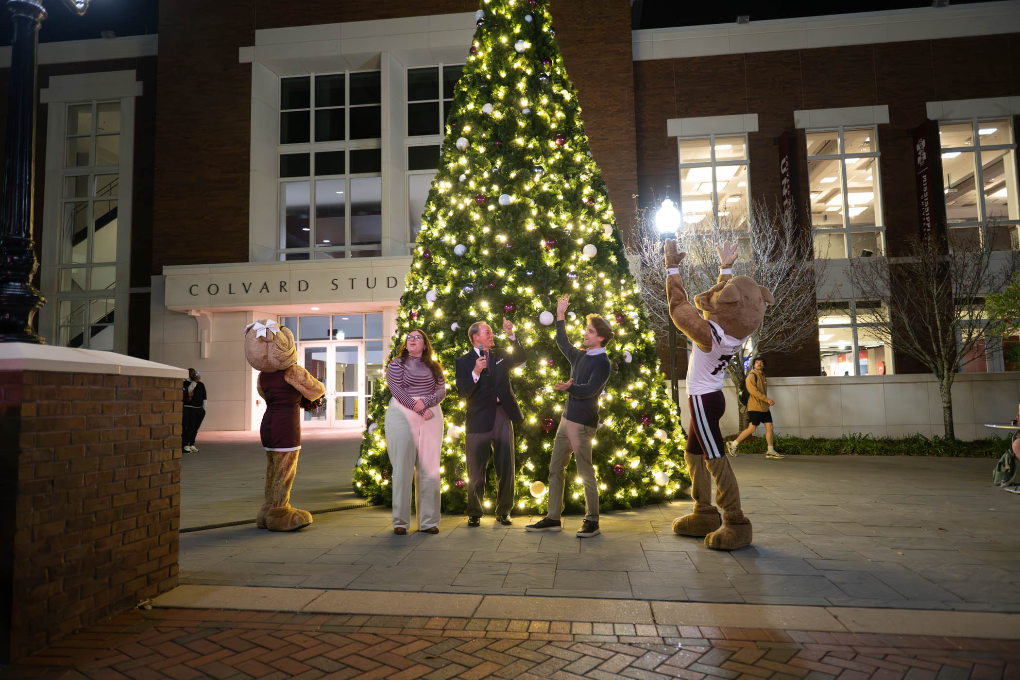 People and bulldog costume mascots in front of lit Christmas tree